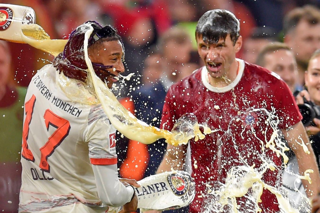 Michael Olise (links) und Thomas Müller bekommen eine Bierdusche: Das kühle Nass gehört zu den Ritualen bei einer Bayern-Meisterfeier.