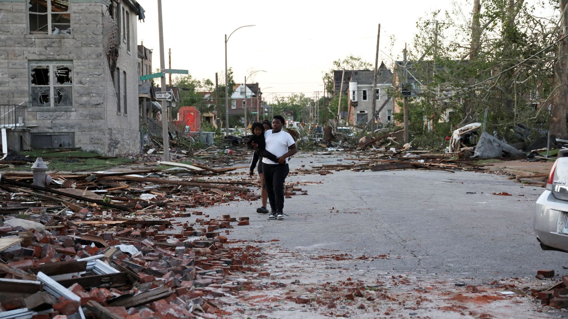 Eine Person trägt ein Kind, während sie durch eine mit Trümmern bedeckte Straße geht, nachdem ein Tornado ihre Nachbarschaft in St. Louis, Missouri, getroffen hat.