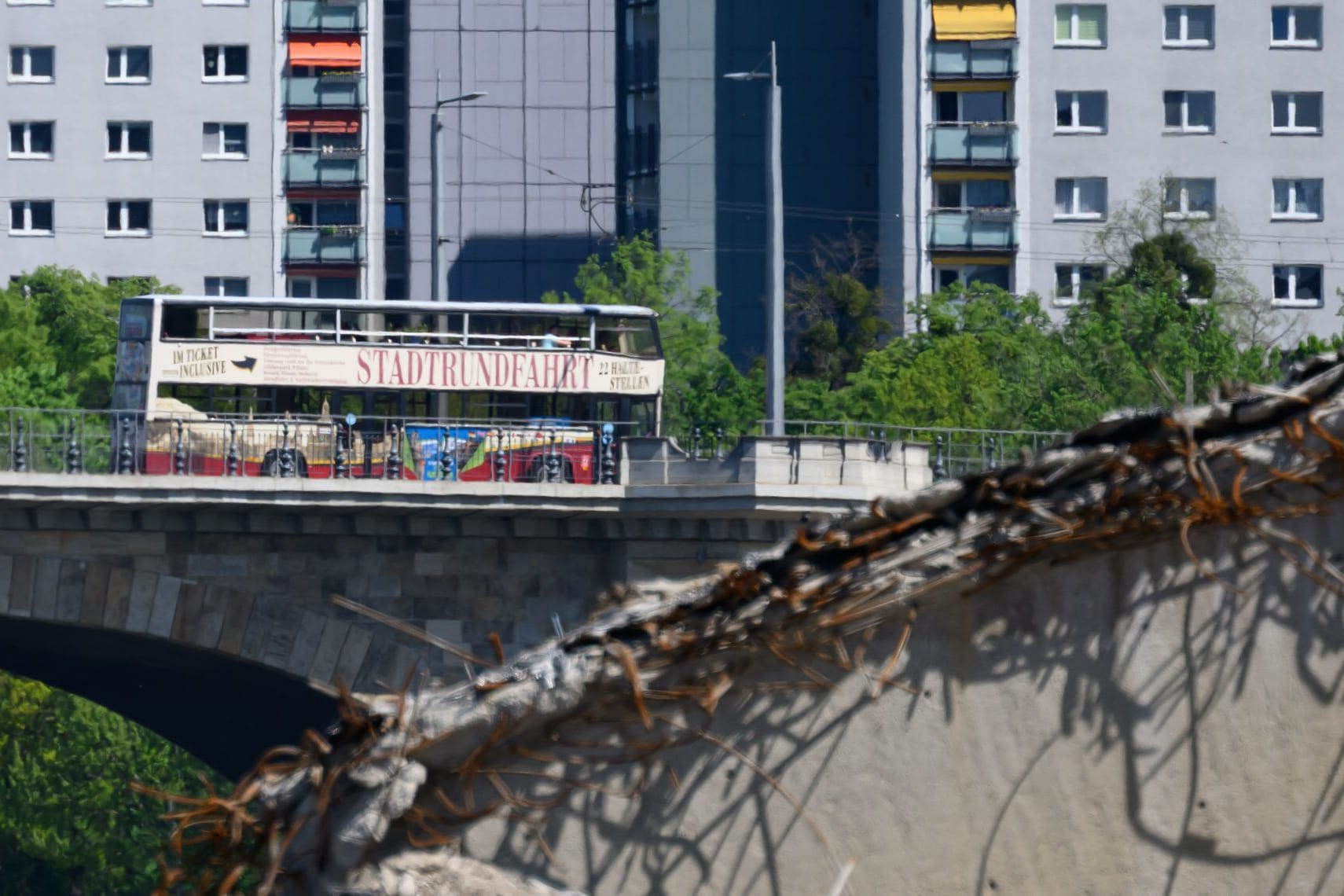 Blick auf den teileingestürzten Brückenzug der Carolabrücke während im Hintergrund ein Bus der Stadtrundfahrt über die Albertbrücke fährt. Ein Teil der 1971 in Betrieb genommenen Brücke mit Straßenbahngleisen und Radweg war in der Nacht zum 11. September 2024 völlig überraschend eingestürzt.