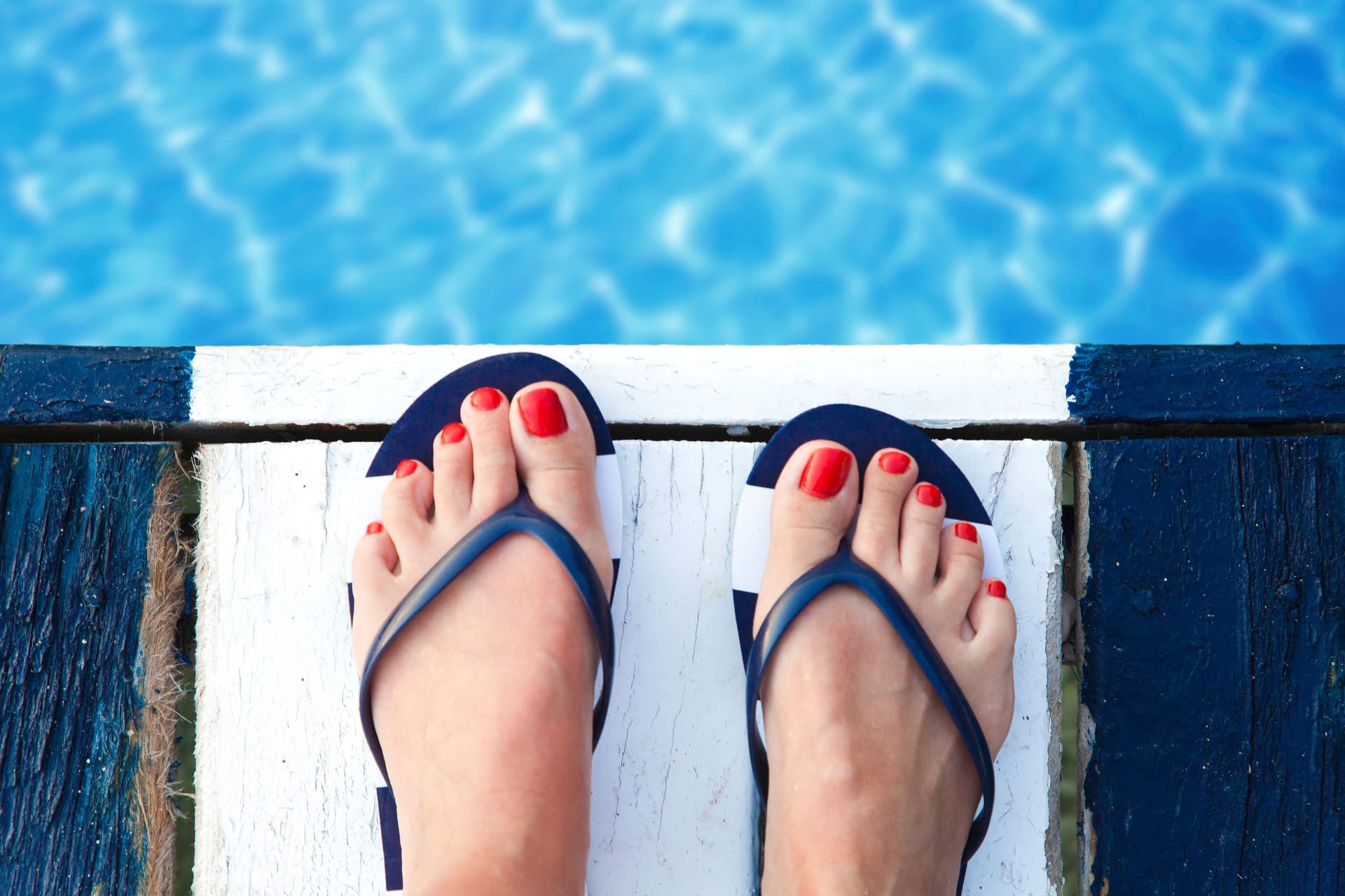 Füße einer Frau in Badeschuhen am Beckenrand: Im Schwimmbad ist das Risiko für Fußpilz erhöht.