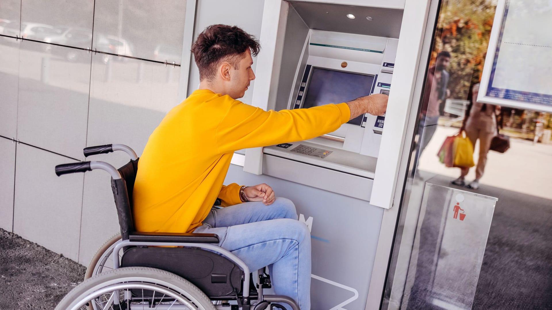 Mann im Rollstuhl hebt Geld ab: Automaten von Banken gehören zu den Produkten, die unter das neue Barrierefreiheitsstärkungsgesetz fallen.