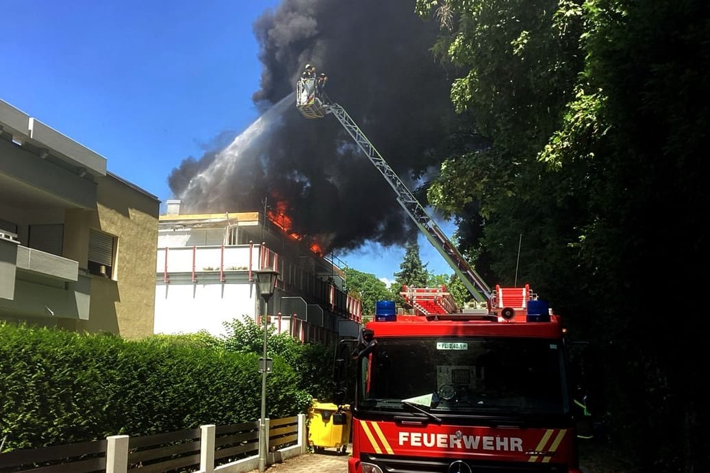 Einsatzkräfte der Feuerwehr löschen den Brand von einer Drehleiter aus: Baustoffe auf dem Dach eines Mehrfamilienhauses standen in Flammen.