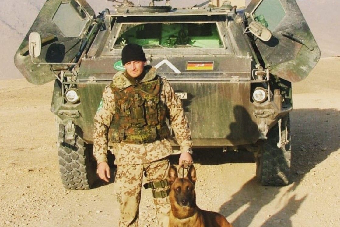 Robert Müller mit seinem Diensthund vor einem gepanzerten Bundeswehr-Fahrzeug im Einsatz in Afghanistan.