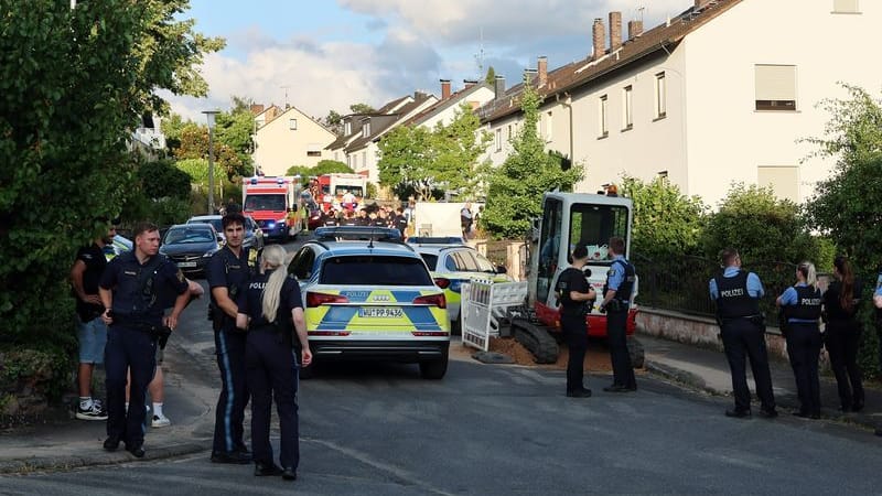 Polizisten stehen an einer Straße, in der Einsatzfahrzeuge von Polizei und Rettungskräften stehen: Ein Mann soll in einem der Häuser am Donnerstag zwei Frauen getötet haben.