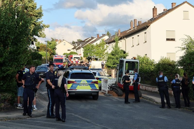 Polizisten stehen an einer Straße, in der Einsatzfahrzeuge von Polizei und Rettungskräften stehen: Ein Mann soll in einem der Häuser am Donnerstag zwei Frauen getötet haben.