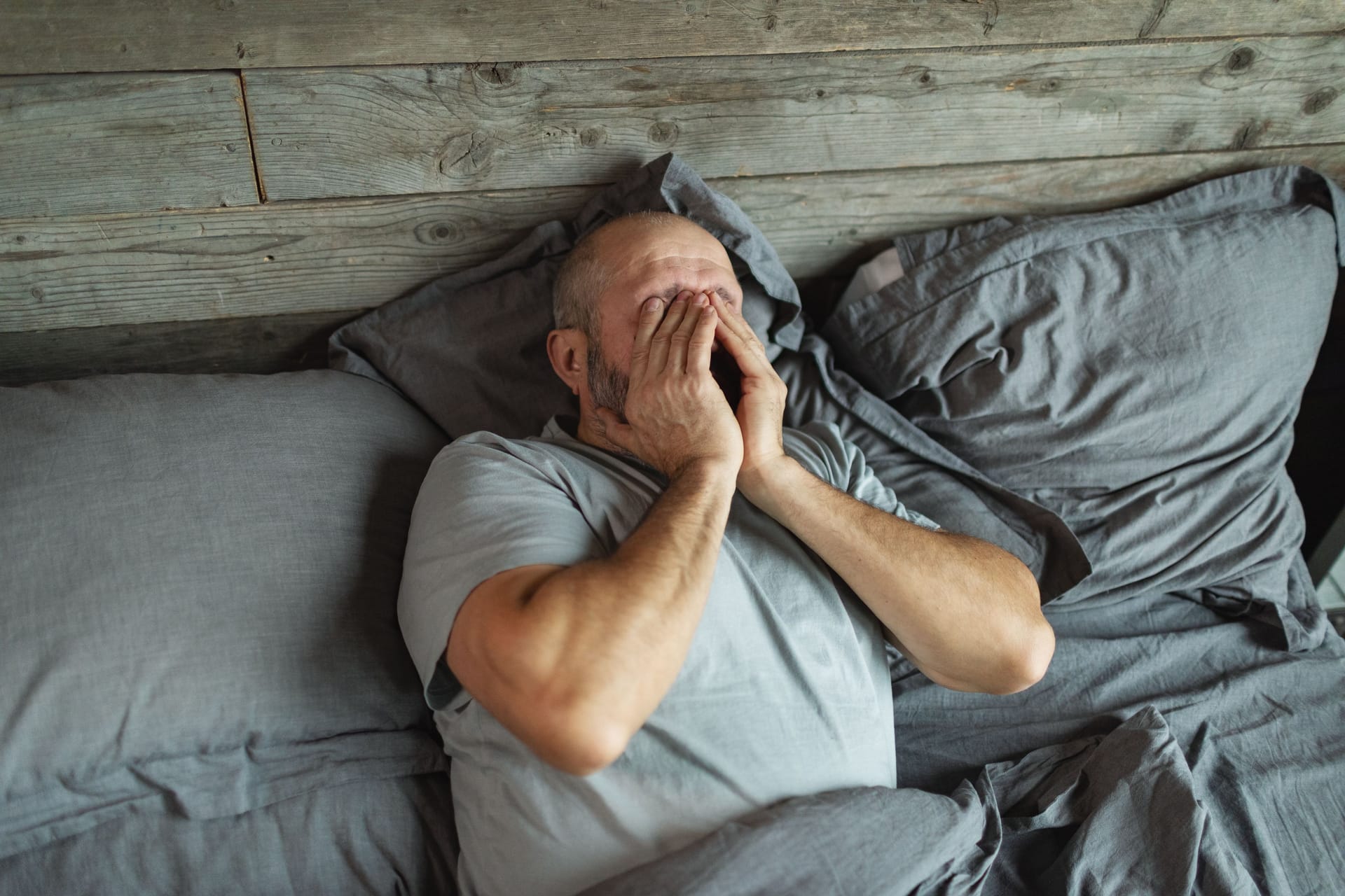 Mann liegt im Bett und ist erschöpft: Neurologische Erkrankungen können sich auf den Schlaf auswirken.