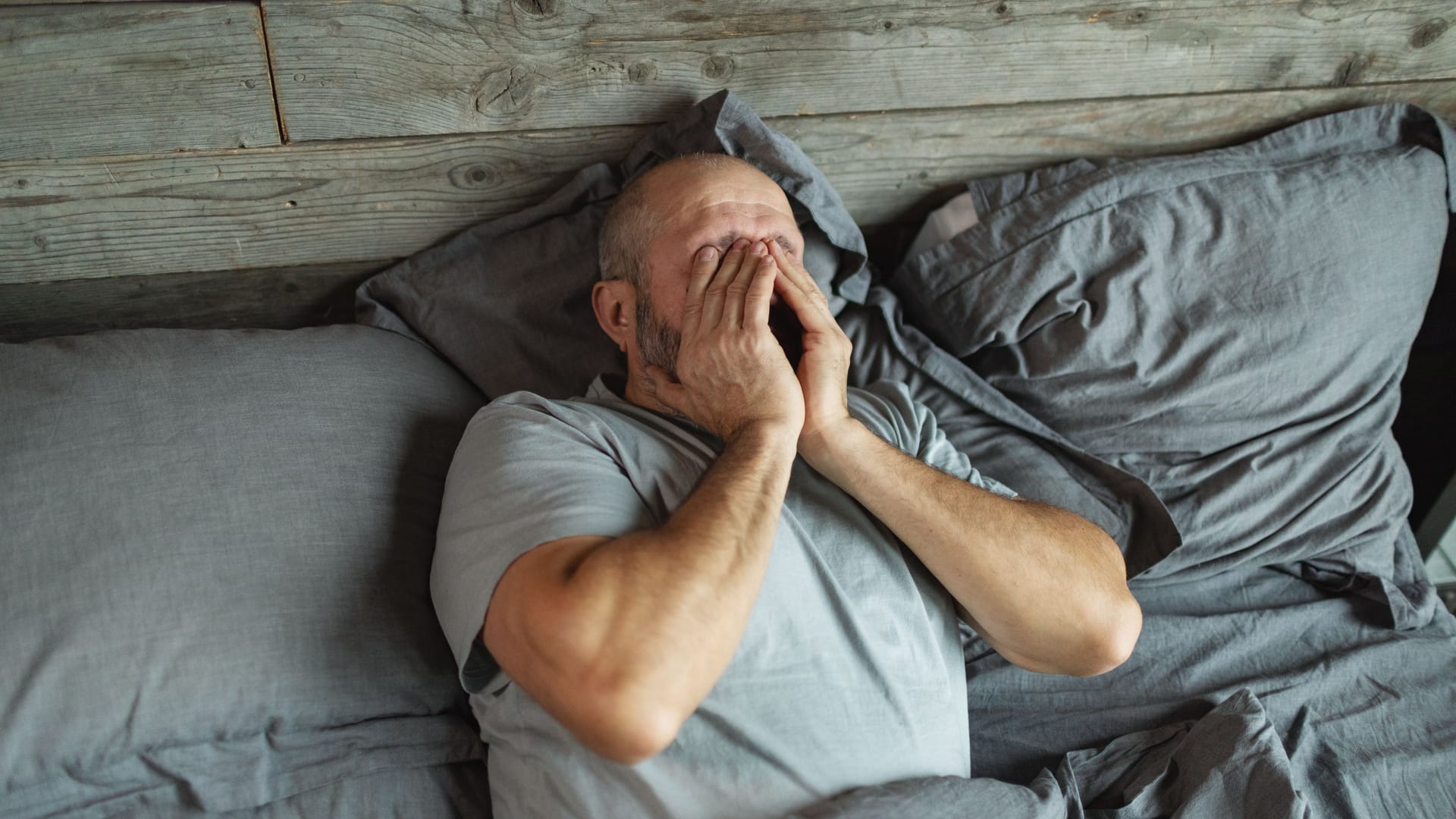 Mann liegt im Bett und ist erschöpft: Neurologische Erkrankungen können sich auf den Schlaf auswirken.