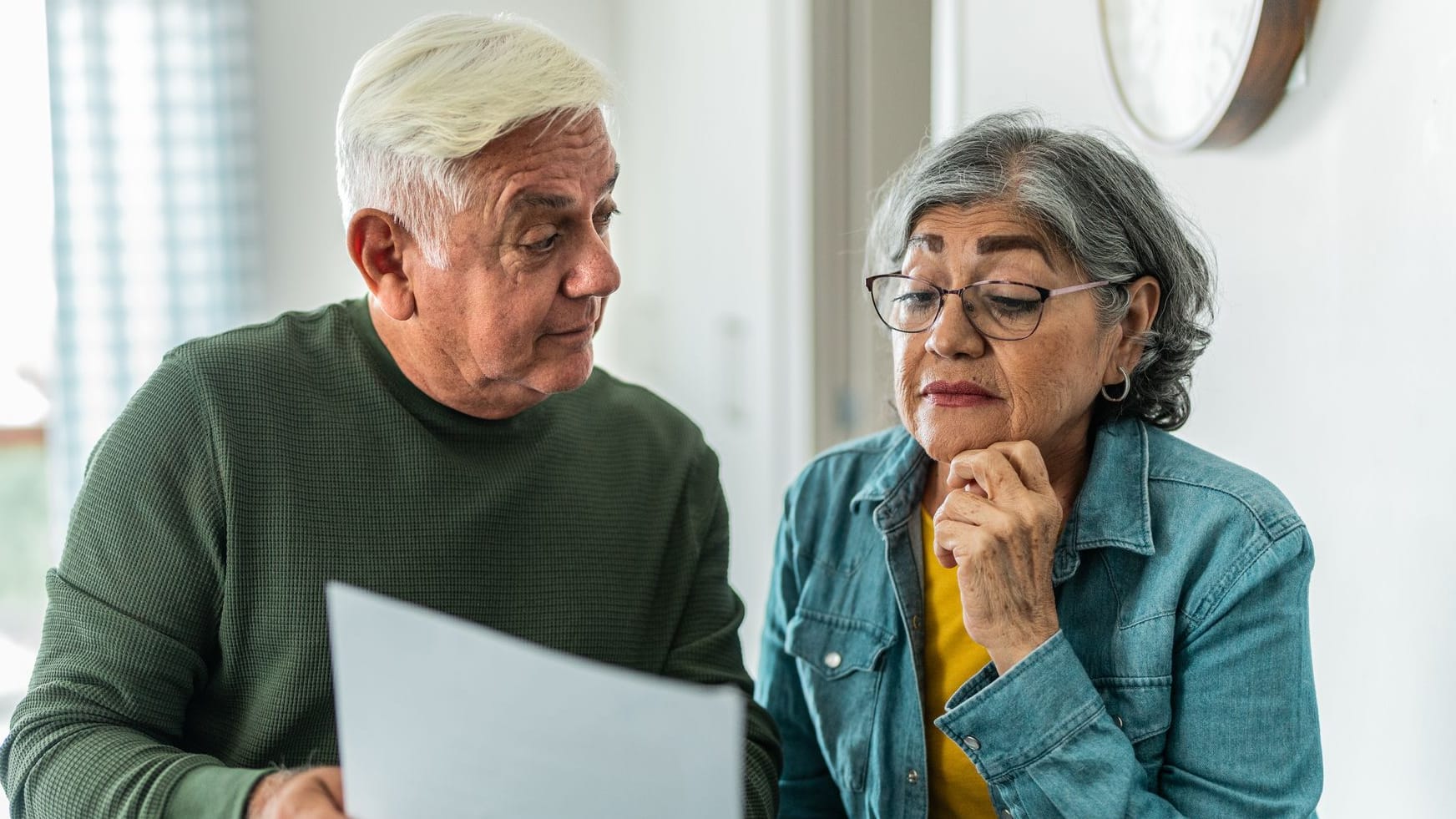 Rentnerpaar liest einen Bescheid: Der gestiegene Pflegebeitrag erreicht Rentner ab Juli 2025.