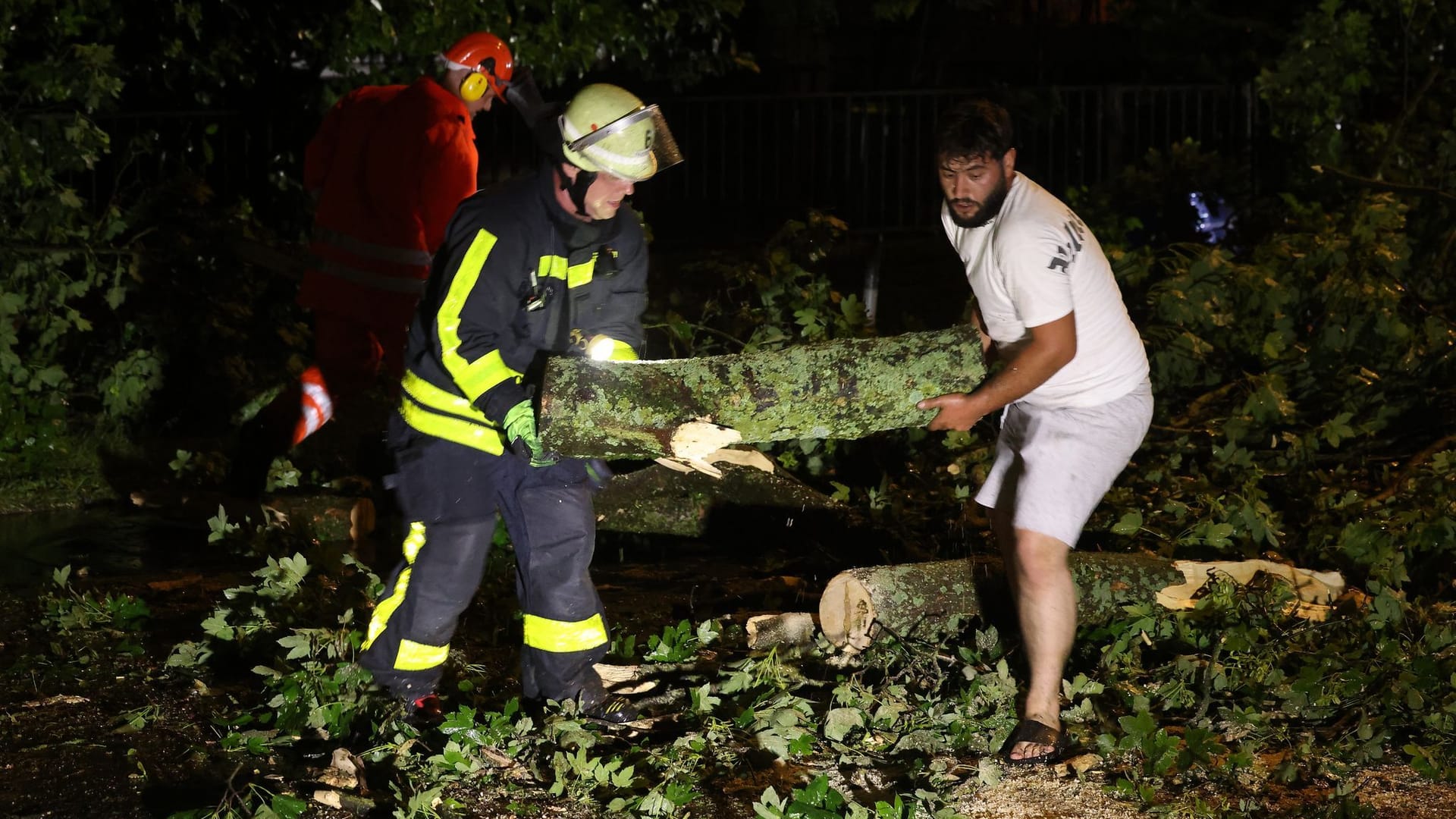 Feuerwehrleute und Anwohner räumen eine Straße mit umgestürzten Bäumen in Krefeld: Unwetter haben Zerstörung angerichtet.