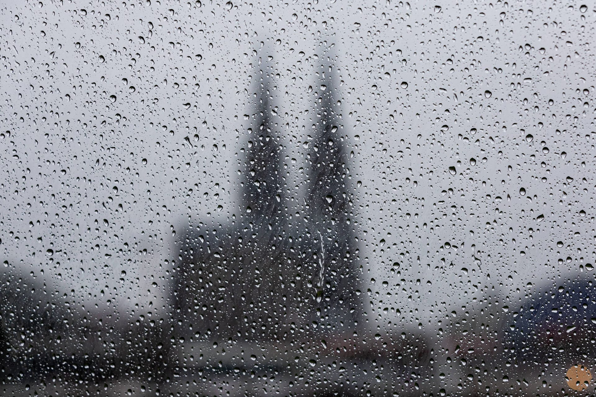 Regentropfen auf eine Glasscheibe, im Hintergrund der Kölner Dom (Archivbild): Der Wochenstart wird ungemütlich am Rhein.