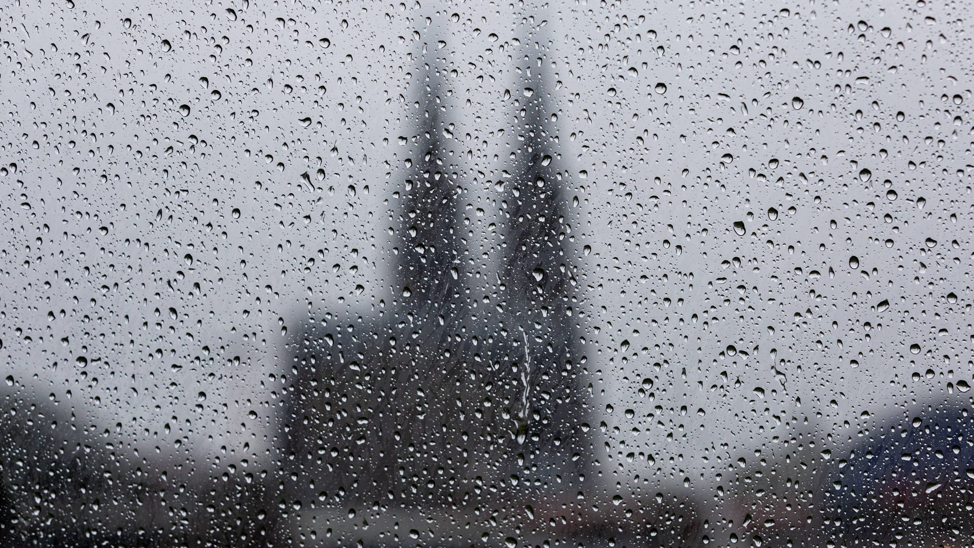 Regentropfen auf eine Glasscheibe, im Hintergrund der Kölner Dom (Archivbild): Der Wochenstart wird ungemütlich am Rhein.