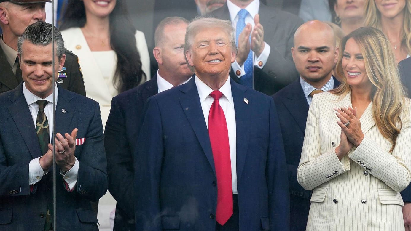 Donald Trump (Mitte) und First Lady Melania Trump sowie Verteidigungsminister Pete Hegseth (l.) sehen sich die Parade zum 250. Geburtstag der US-Armee an.