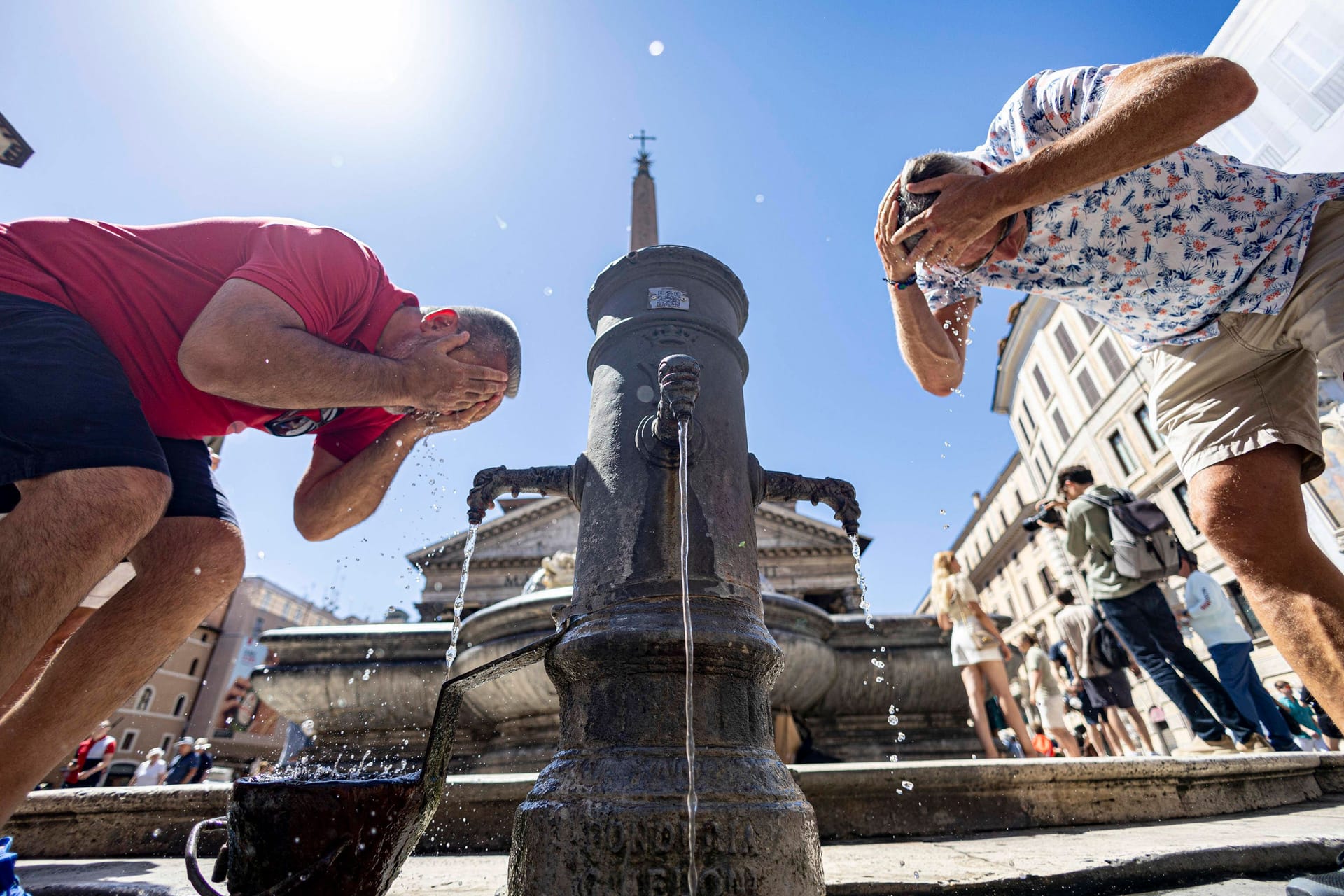 Sommer in Rom: Zwei Männer erfrischen sich an einem öffentlichen Wasserspender.