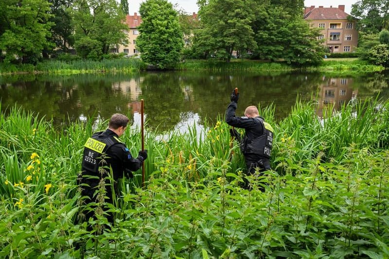 Polizeibeamte suchen das Ufer des Breitkopfbeckens in Reinickendorf mit langen Stangen und Metalldetektoren ab. Gesucht wird nach Gegenständen, die mit dem Mord an einem 50-jährigen Mann in Zusammenhang stehen können.
