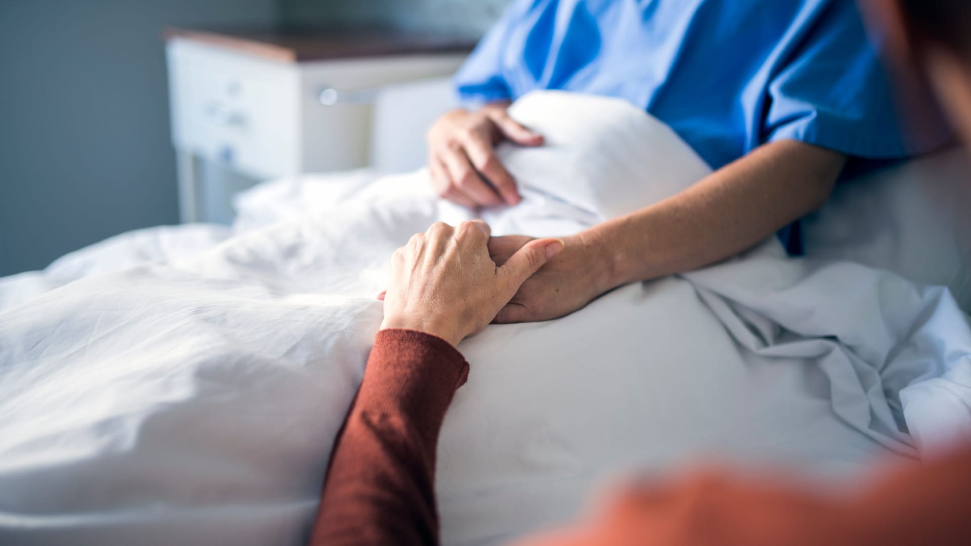 Eine Person hält die Hand eines im Bett liegenden Mannes: Bei Speiseröhrenkrebs im Endstadium ist eine sogenannte palliative Therapie angebracht.