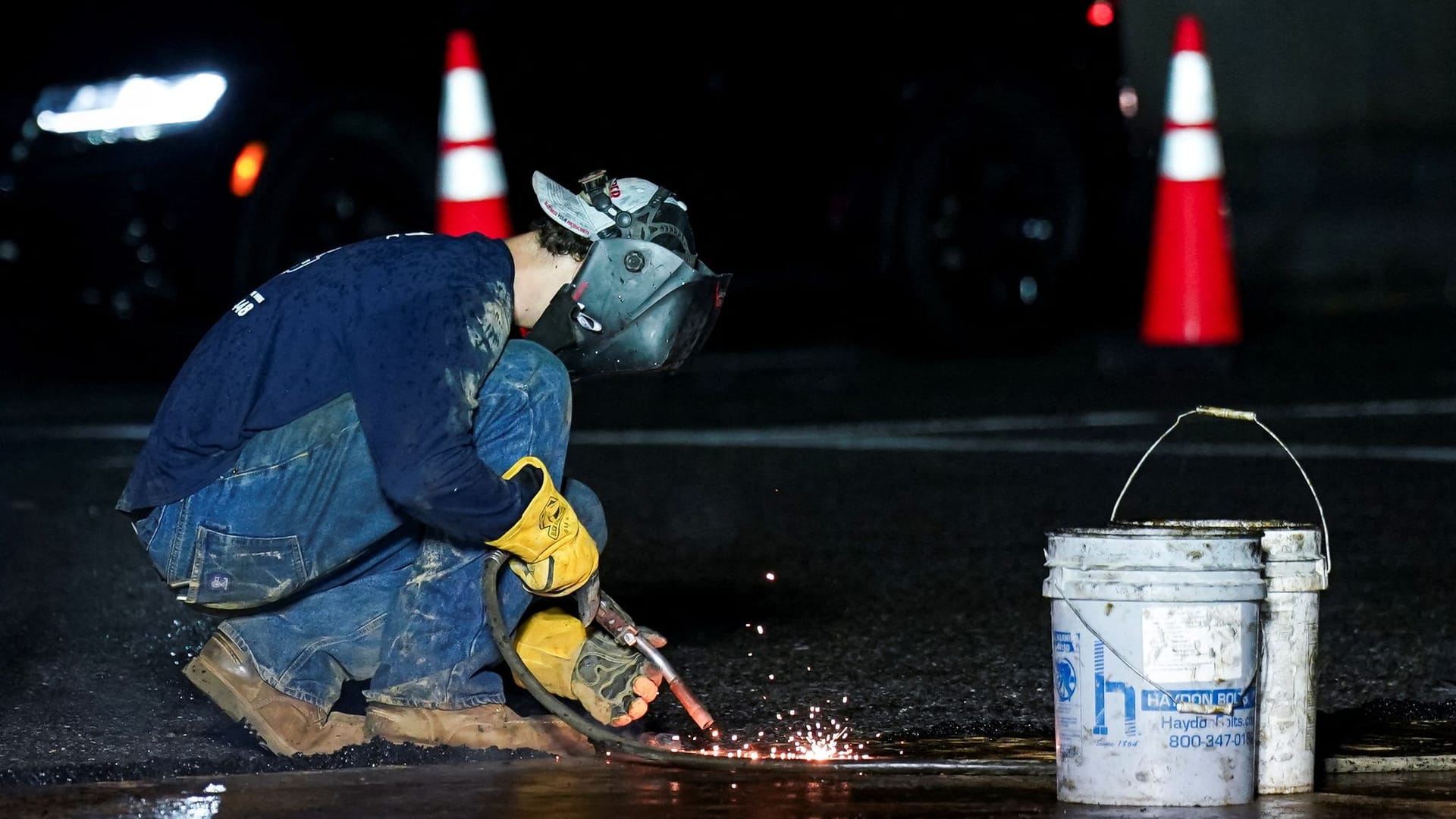 A worker welds a metal plate to protect the street from damage by military vehicles ahead of the U.S. Army's 250th Birthday Festival and Parade in Washington