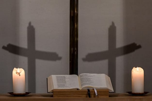 Kerzen, eine Bibel, ein Kreuz und die Schatten des Kreuzes sind in einer Kapelle zu sehen (Symbolbild):