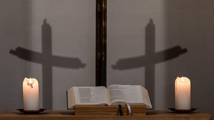 Kerzen, eine Bibel, ein Kreuz und die Schatten des Kreuzes sind in einer Kapelle zu sehen (Symbolbild): Kerzen, eine Bibel, ein Kreuz und die Schatten des Kreuzes sind in einer Kapelle zu sehen (Symbolbild):