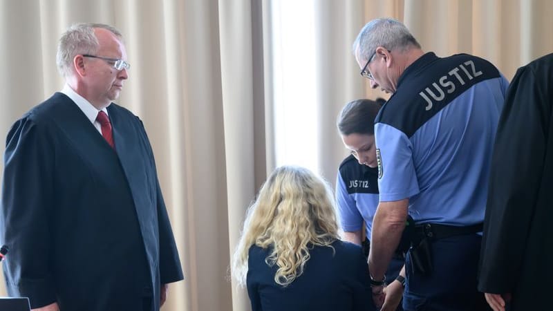 Die Hauptangeklagte (M) sitzt vor Beginn des Prozesses gegen eine 52 Jahre alte Frau und einen 76 Jahre alten Mann wegen Mordes und Beihilfe in einem Verhandlungssaal im Landgericht, daneben stehen ihre Rechtsanwälte Ulf Israel (l) und Andrej Klein.