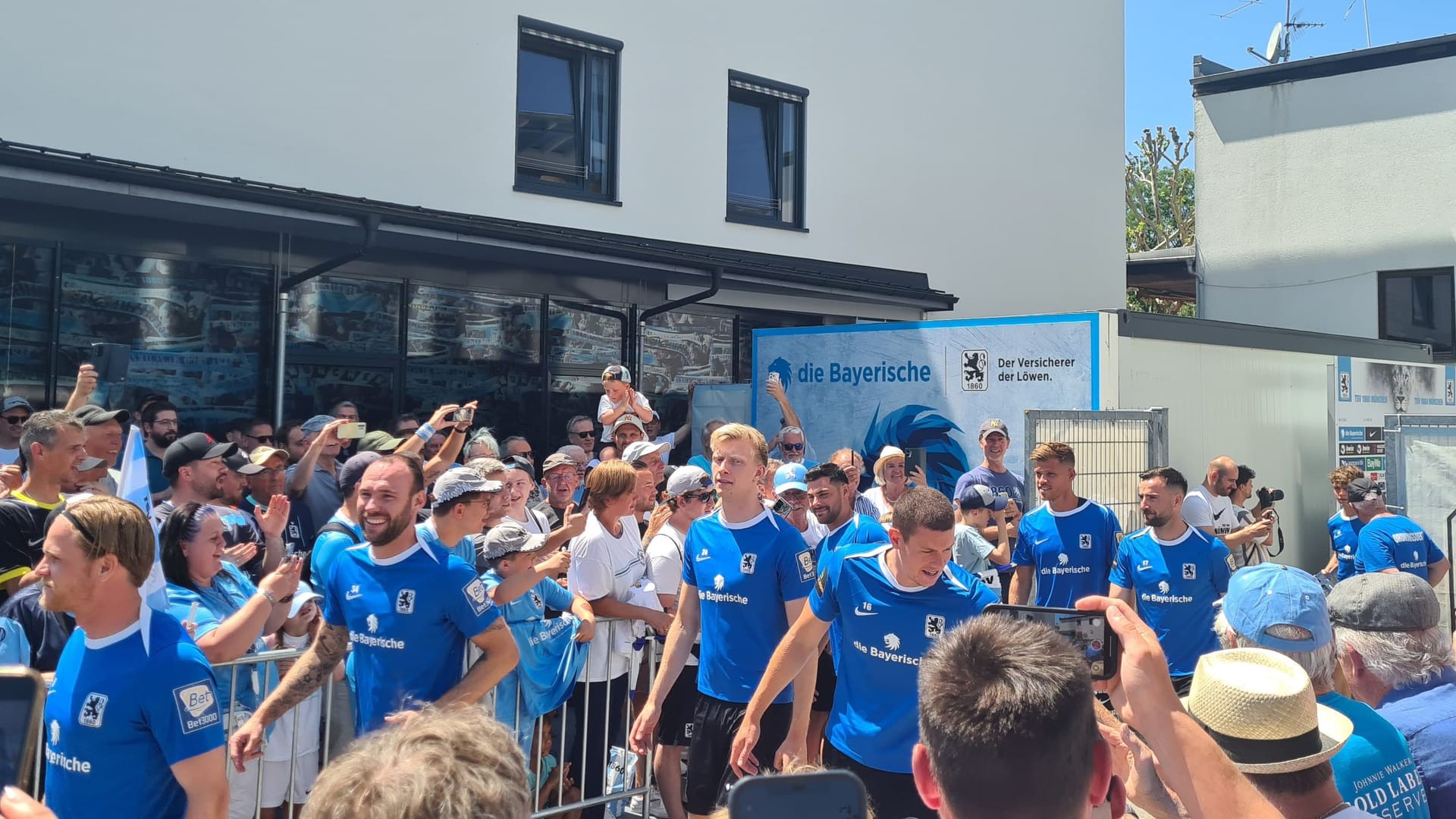Die Mannschaft von 1860 München auf dem Weg zum Trainingsplatz: Hunderte Fans stehen in der Mittagshitze Spalier.