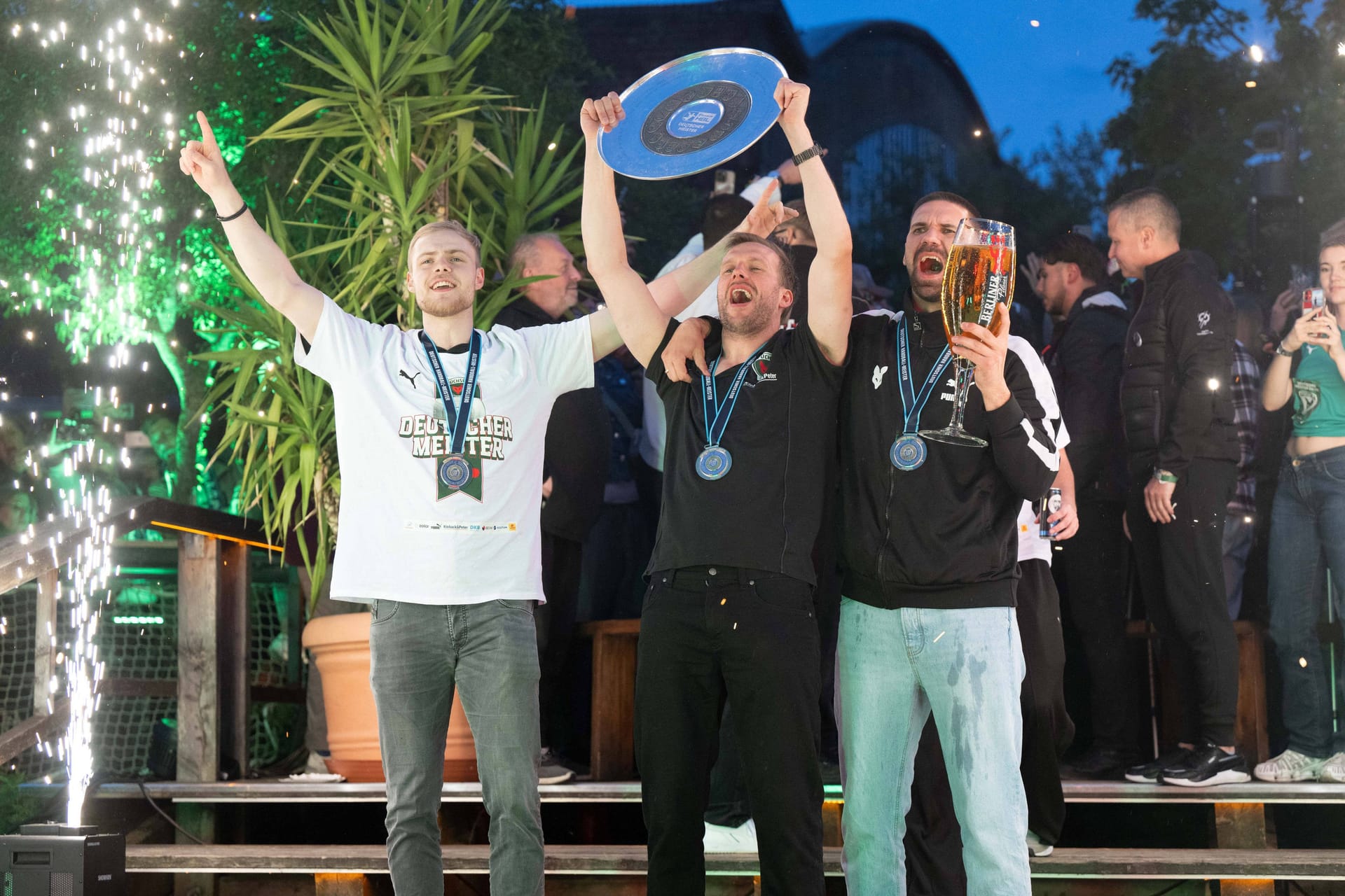 Die Meisterfeier der Füchse Berlin nach der Rückkehr aus Mannheim: Max Darj (m.) feiert mit Schale, Fabian Wiede (r.) mit einem großen Glas Bier.