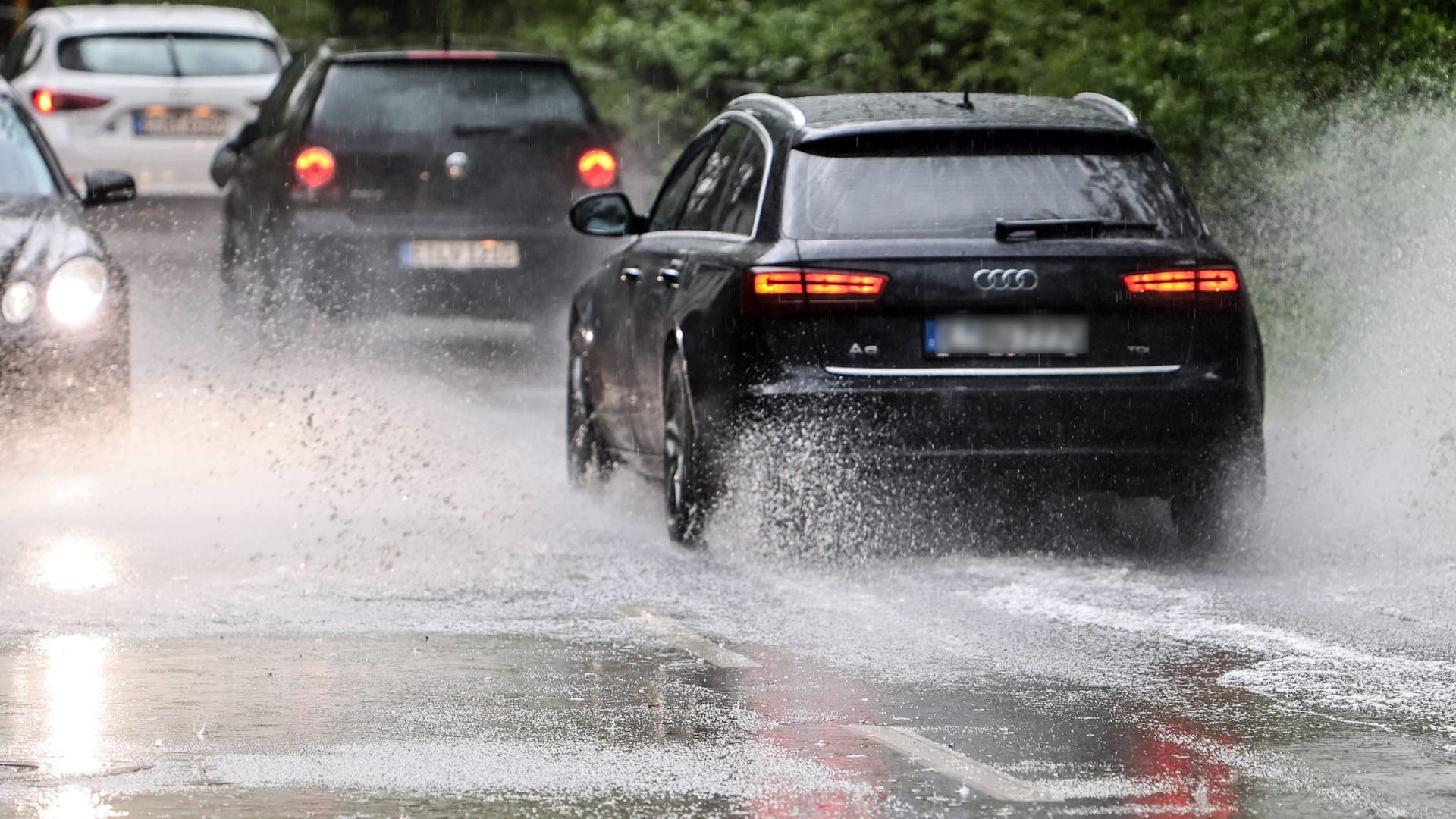 Autos fahren über eine überflutete Straße (Symbolbild): In Köln und der Region werden am Wochenende Starkregen und Unwetter erwartet.