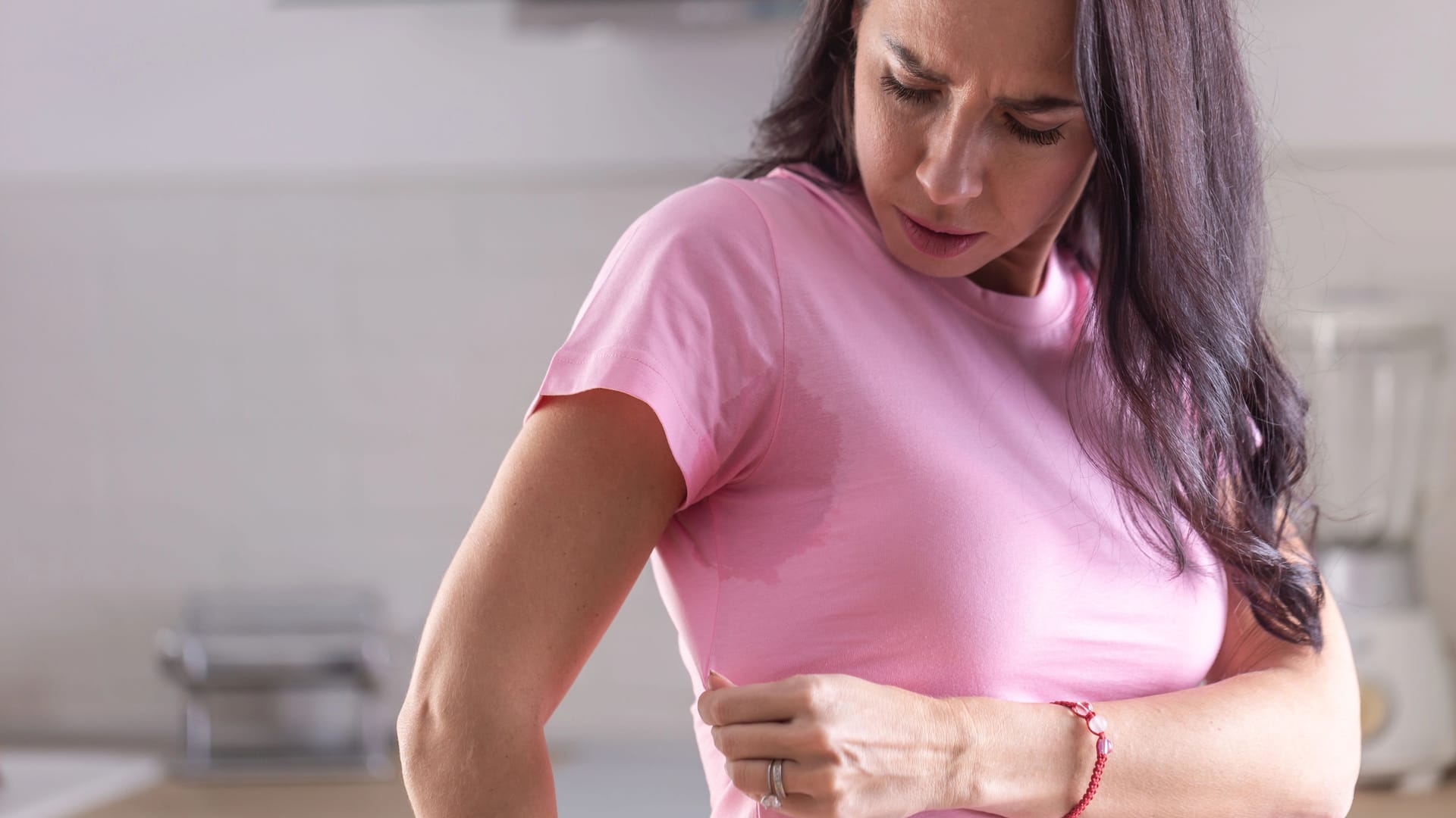 Excessive sweating visible by stains on a pink shirt of a young woman