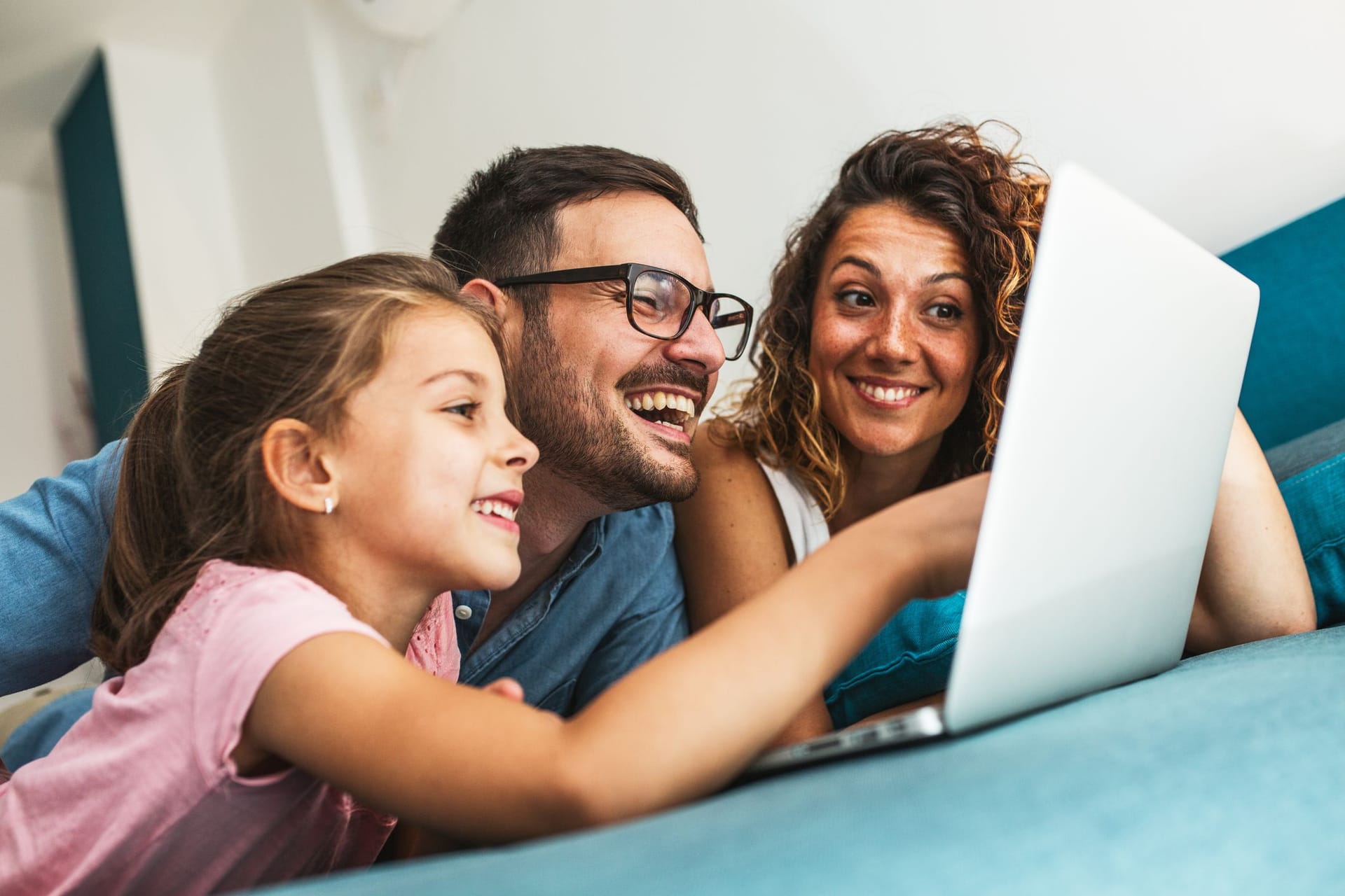 Familie liegt auf dem Bett und schaut auf einen Laptop-Bildschirm