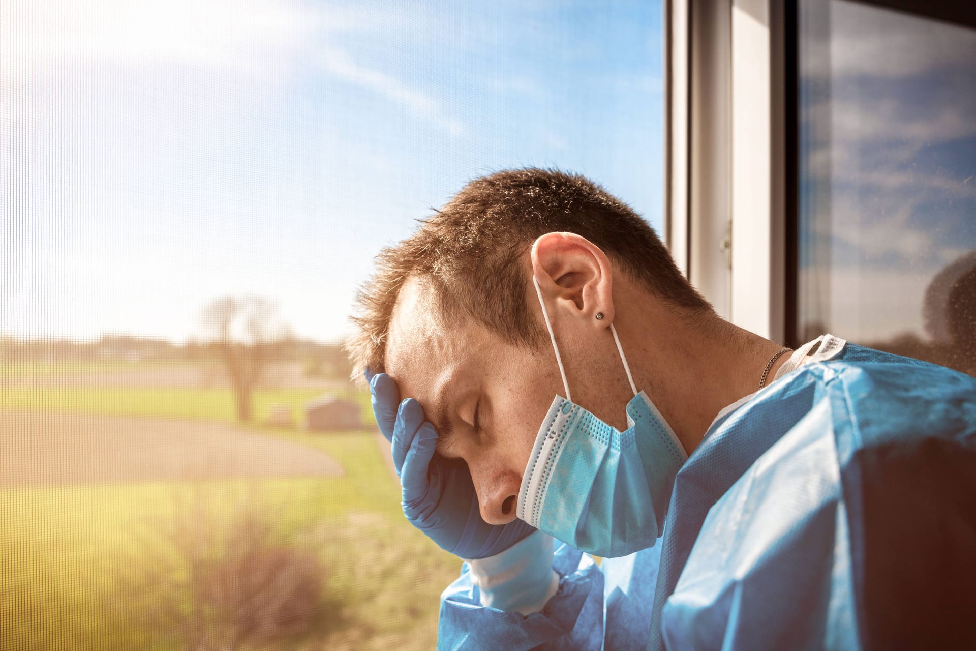 Pflegekraft erschöpft am Fenster (Symbolbild): Für die Pflegeeinrichtungen und Kliniken wird die Sommerhitze zur Herausforderung.