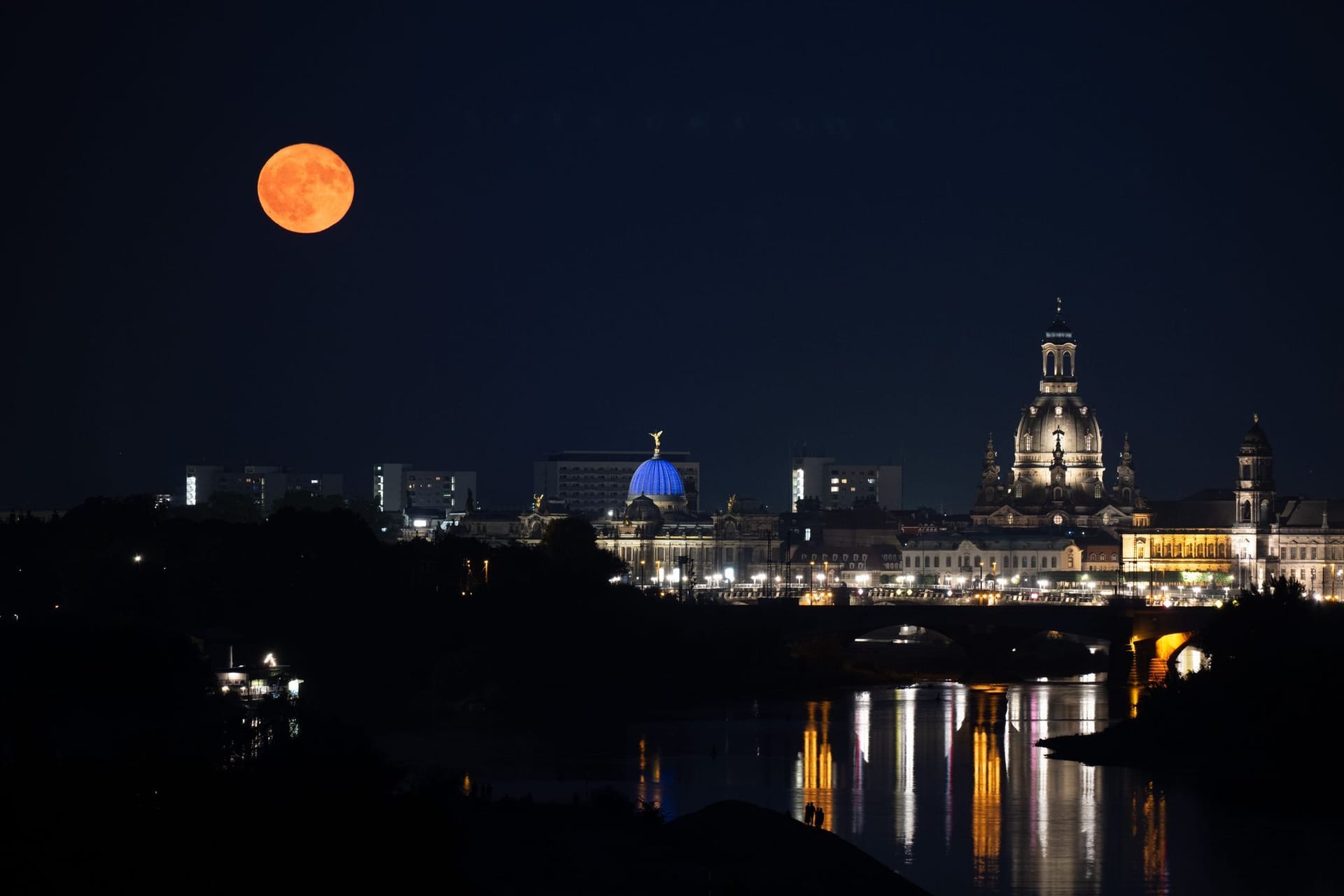Passanten beobachten am Ufer der Elbe vor der Kulisse der Altstadt den Aufgang des Erdbeermond.