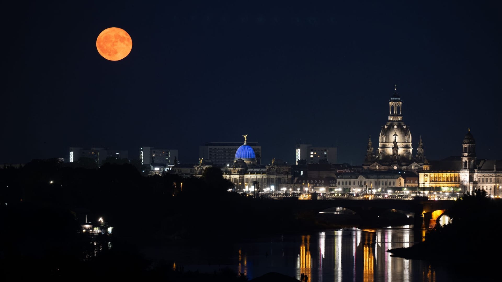 Passanten beobachten am Ufer der Elbe vor der Kulisse der Altstadt den Aufgang des Erdbeermond.