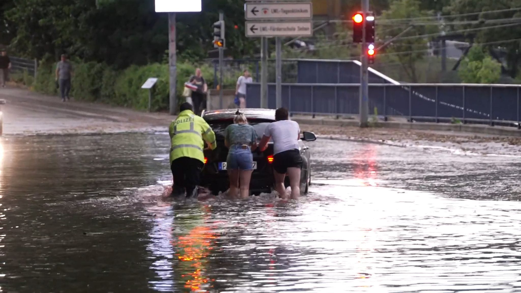 Menschen schieben ein Auto durch eine überflutete Straße in Paderborn.