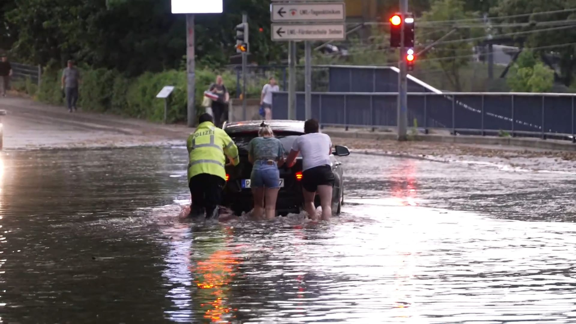 Menschen schieben ein Auto durch eine überflutete Straße in Paderborn.