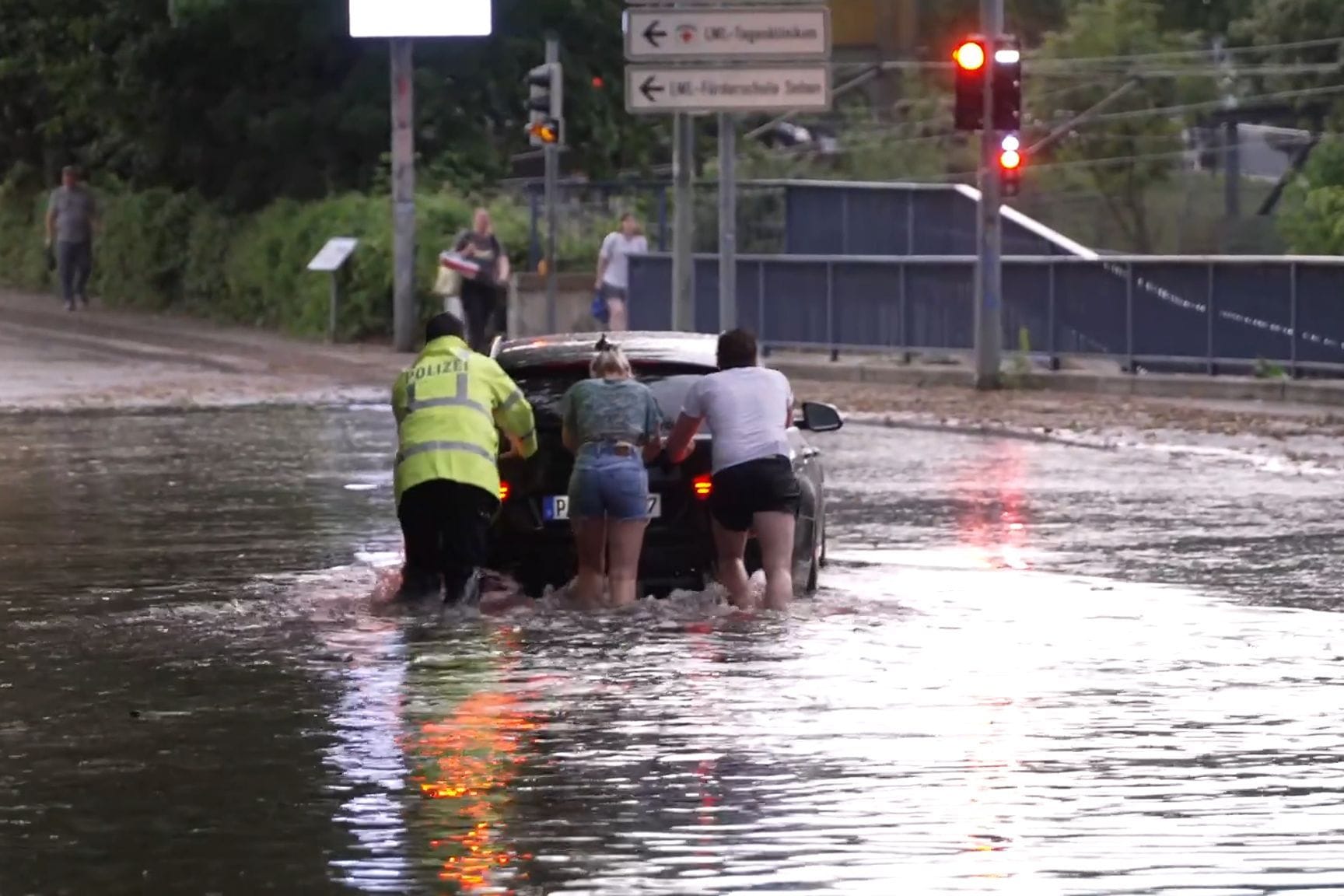 Menschen schieben ein Auto durch eine überflutete Straße in Paderborn.