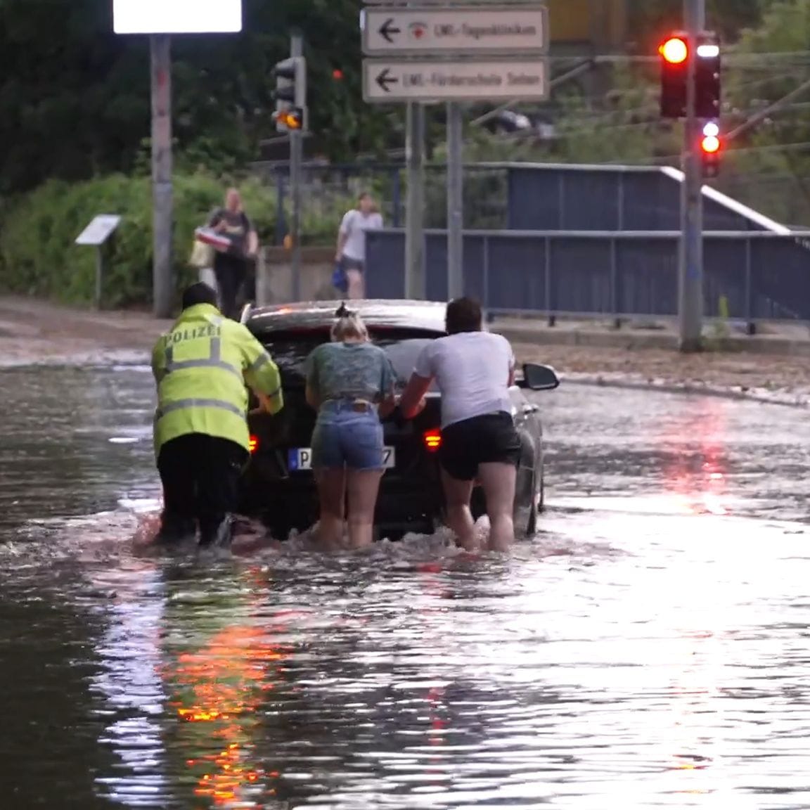 Menschen schieben ein Auto durch eine überflutete Straße in Paderborn.