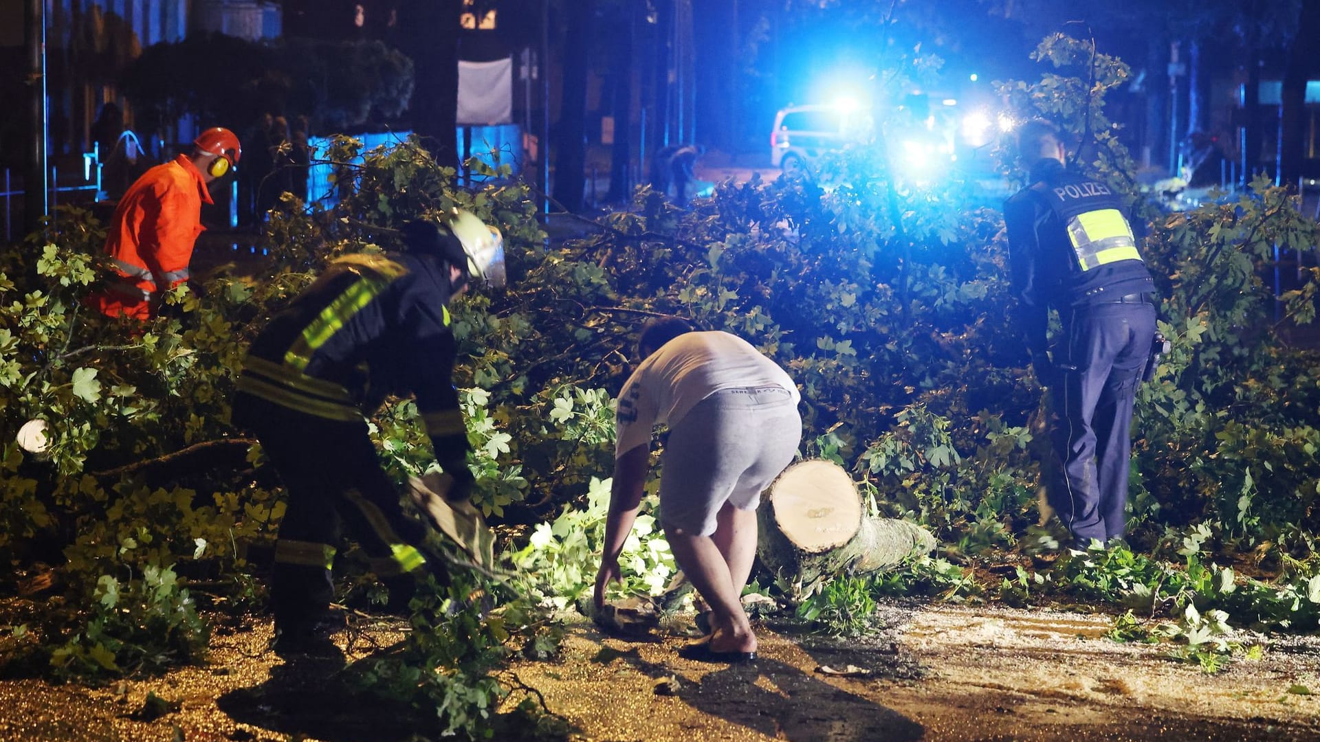 Feuerwehrleute räumen eine Straße mit umgestürzten Bäumen in Krefeld: Heftige Unwetter haben immense Schäden angerichtet.