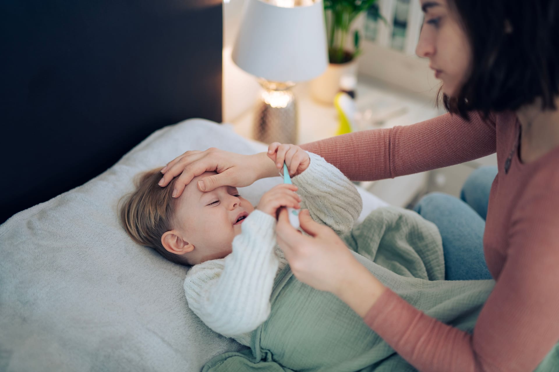 Besorgte Mutter prüft die Temperatur ihres Kindes: Bei einer Hib-Infektion kann es zu Fieber kommen.