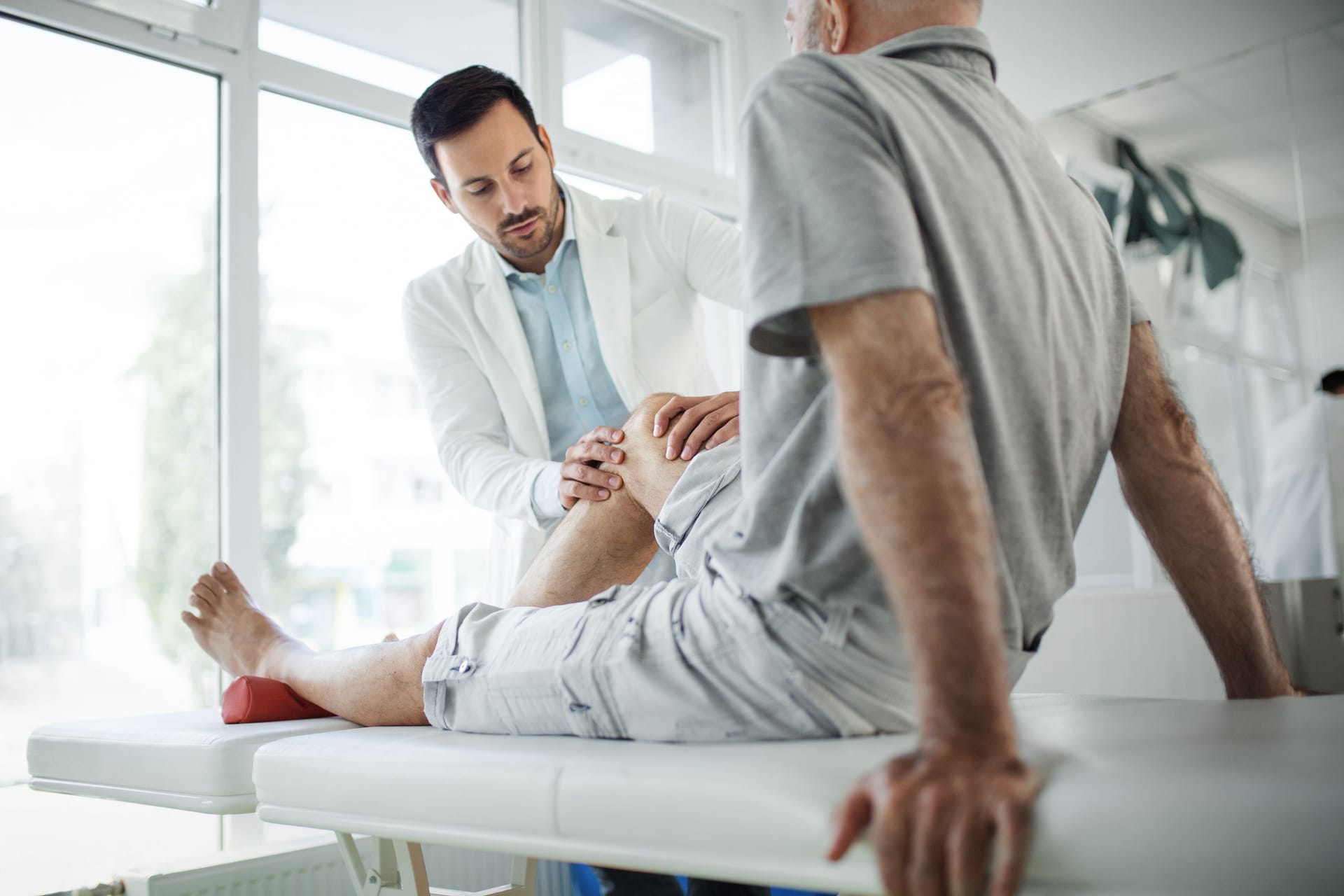 Arzt untersucht das Knie eines Patienten: Ein mögliches Anzeichen von Knochenkrebs sind Bewegungseinschränkungen.