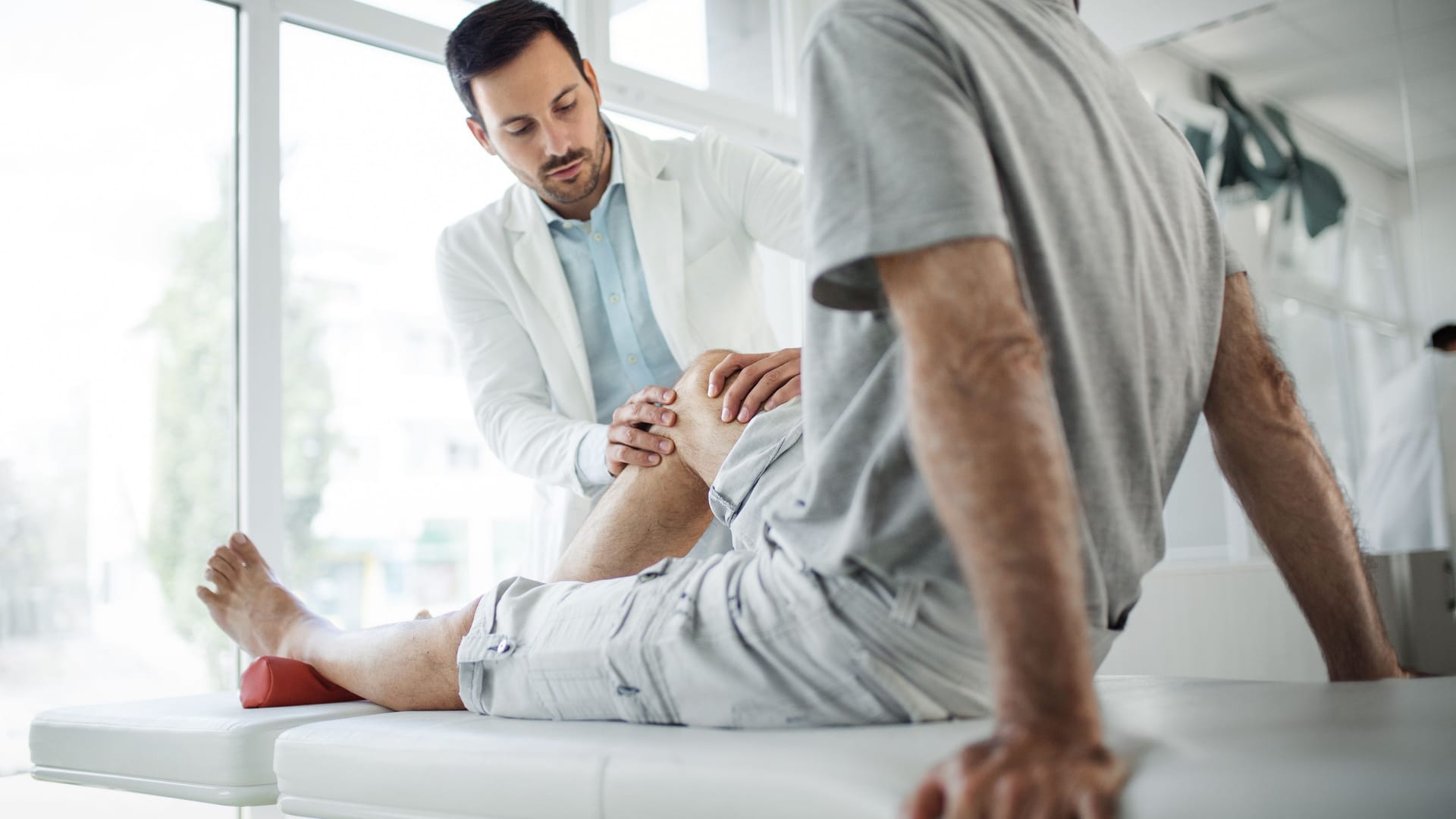 Arzt untersucht das Knie eines Patienten: Ein mögliches Anzeichen von Knochenkrebs sind Bewegungseinschränkungen.
