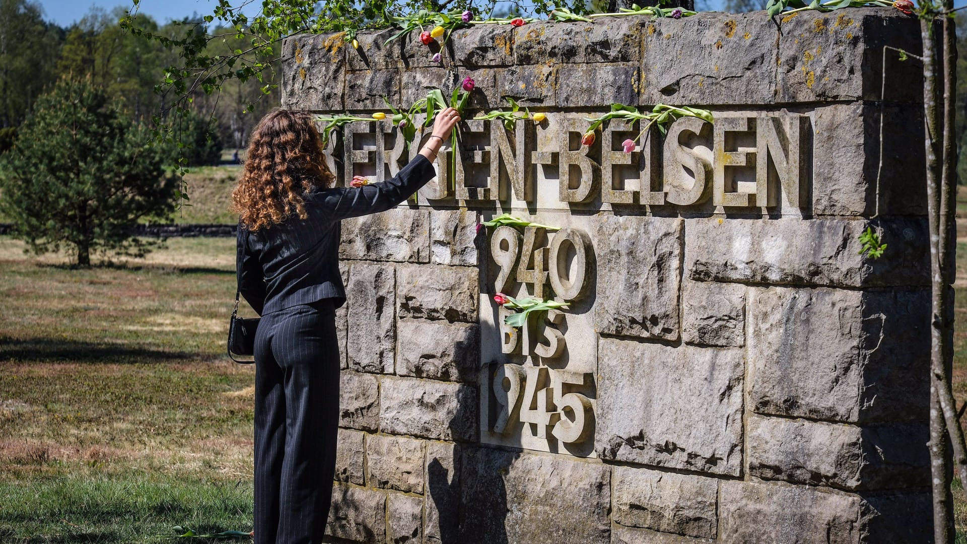Eine Frau legt eine Blume auf dem Schriftzug "Bergen-Belsen" nieder (Archivbild): Die NS-Gedenkstätte veranstaltet am 22. Juni erstmals eine Führung auf Deutsch und Russisch.