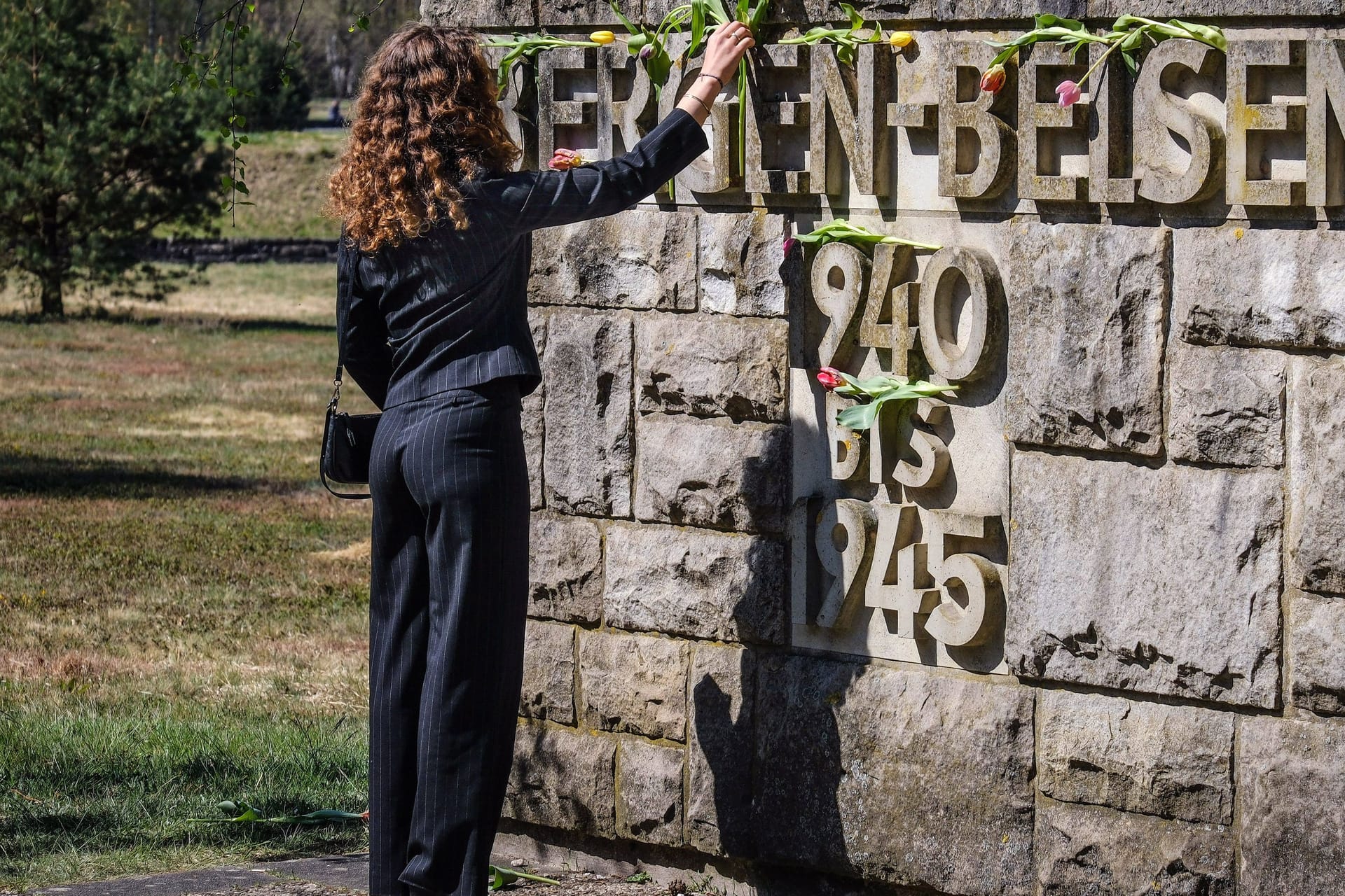Eine Frau legt eine Blume auf dem Schriftzug "Bergen-Belsen" nieder (Archivbild): Die NS-Gedenkstätte veranstaltet am 22. Juni erstmals eine Führung auf Deutsch und Russisch.
