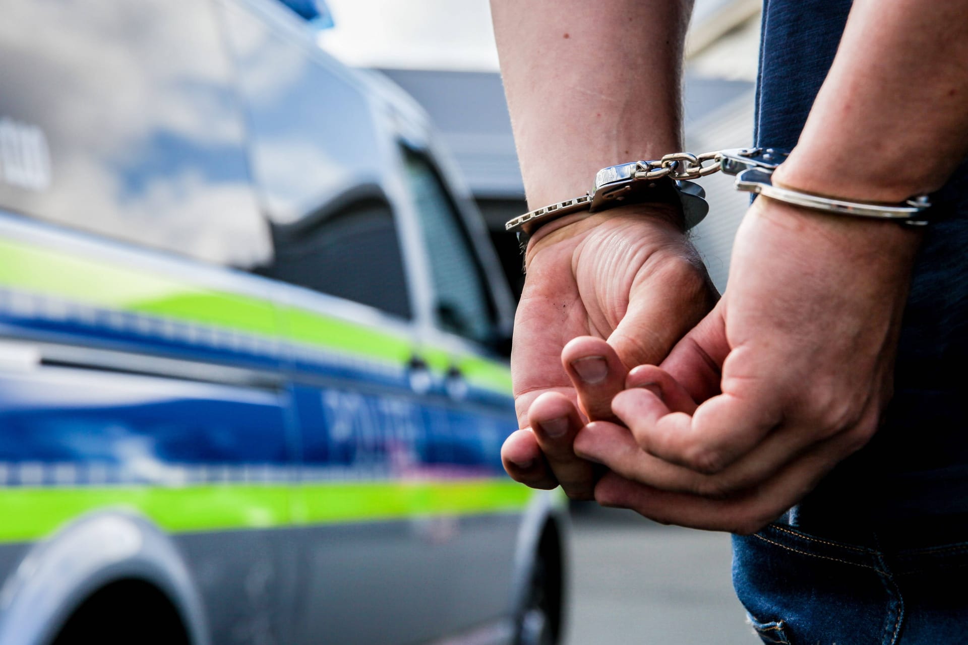 Person in Handschellen neben einem Polizeifahrzeug (Symbolbild): Der Mann soll insgesamt zwölf Diebstähle begangen haben.