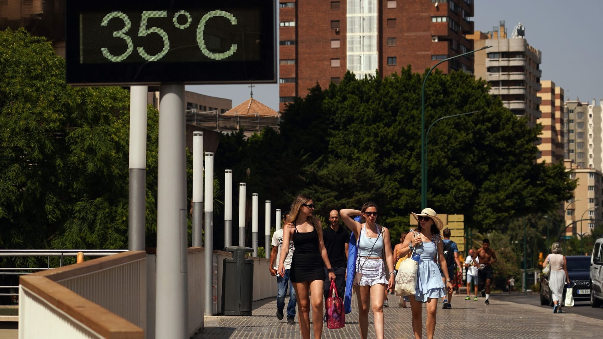 Menschen gehen in der südspanischen Stadt Málaga an einem Thermometer vorbei, das 35 Grad anzeigt.