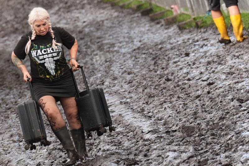 Metal-Fans tragen ihr Gepäck über das Festivalgelände des Wacken Open Air: Massive Regenfälle haben das Areal zu einer Matschfläche gemacht.