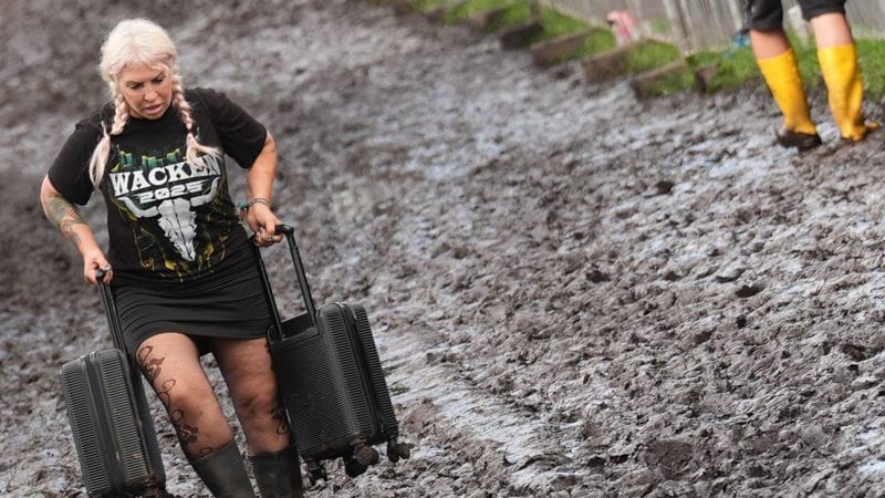 Metal-Fans tragen ihr Gepäck über das Festivalgelände des Wacken Open Air: Massive Regenfälle haben das Areal zu einer Matschfläche gemacht.