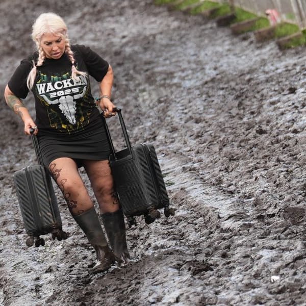 Metal-Fans tragen ihr Gepäck über das Festivalgelände des Wacken Open Air: Massive Regenfälle haben das Areal zu einer Matschfläche gemacht.