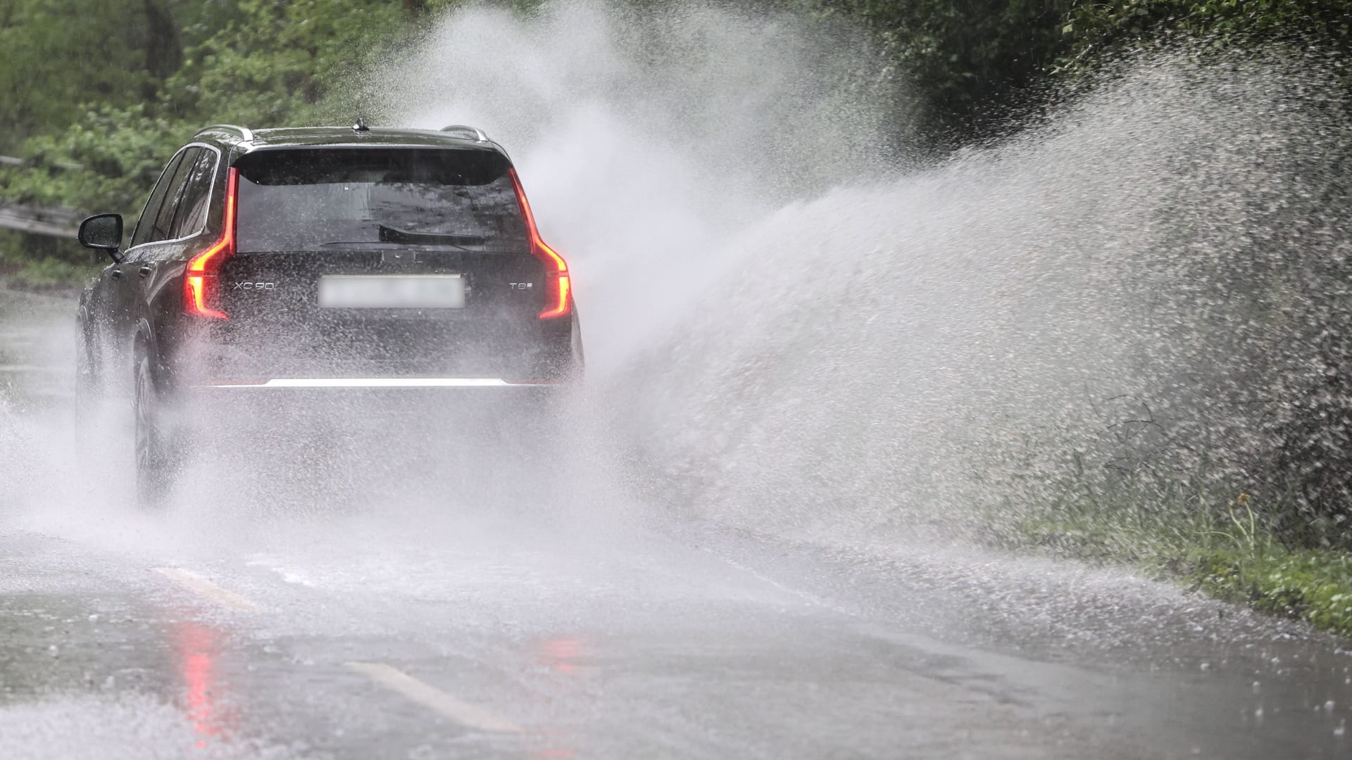 Ein Auto fährt bei Starkregen über eine überschwemmte Straße (Archivbild): In Köln und der Region drohen am Donnerstag neue Unwetter – danach wird es kalt.