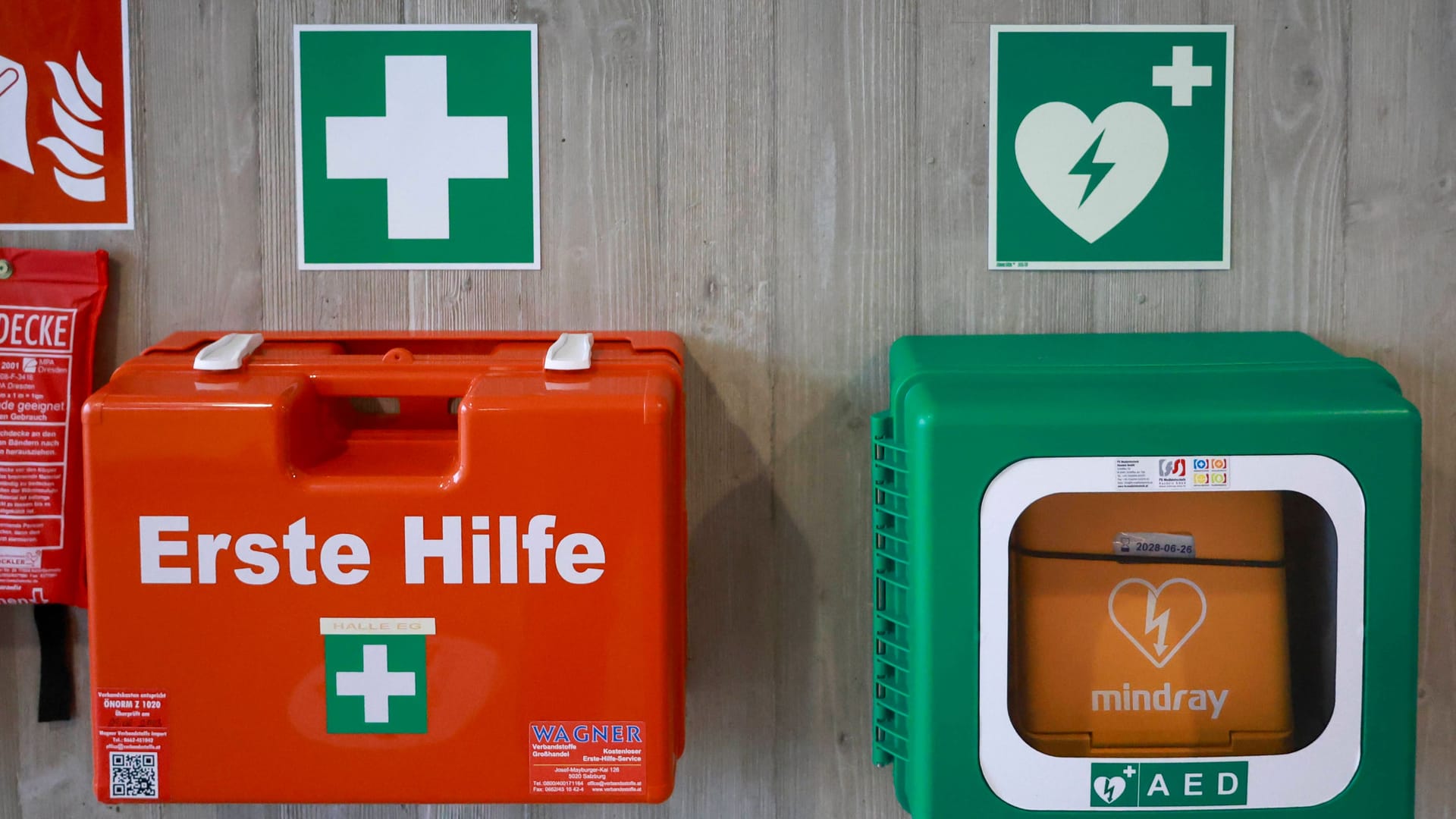 Grünes Schild, weißes Kreuz: Hier hängt der Erste-Hilfe-Kasten.