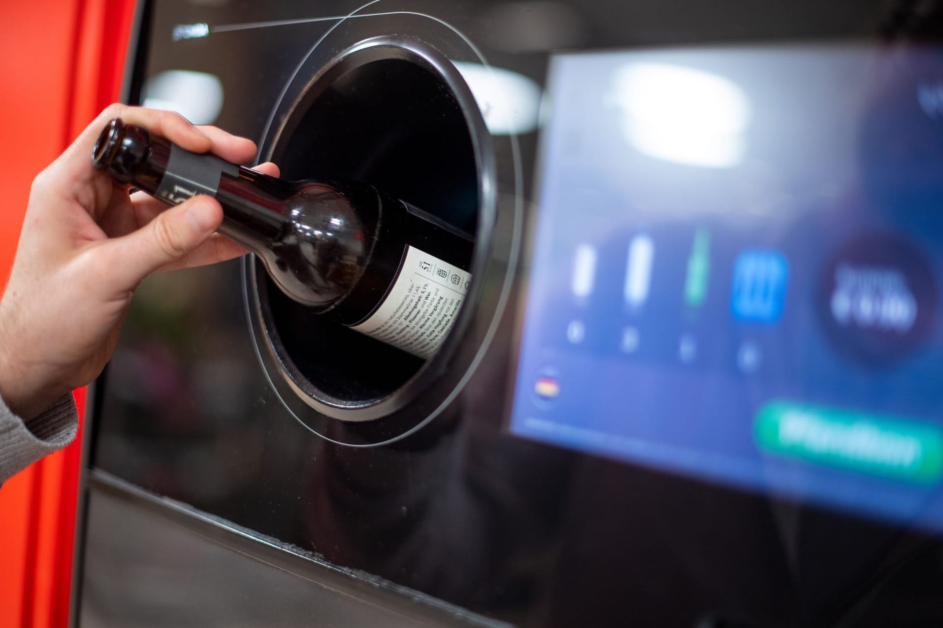 Person gibt eine Flasche in einen Leergutautomaten