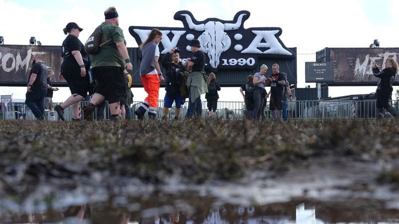 Metal-Fans gehen über das teilweise matschige Festivalgelände des Wacken Open Airs.